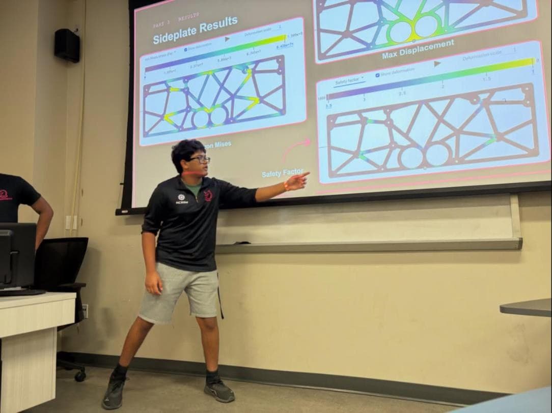 A RoboKnights presenter pointing to sideplate stress, displacement, and safety factor results